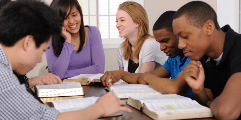 A diverse group of students in a Christian school setting, perhaps in a classroom or outdoor space, engaging with one another respectfully.