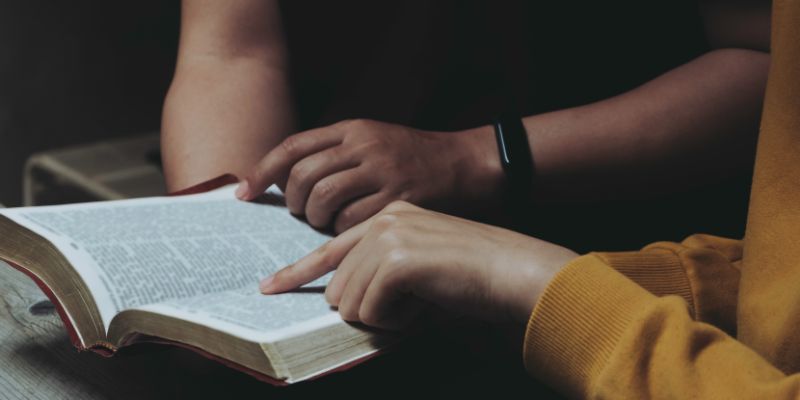 An image of two young people in a thoughtful conversation, standing in a peaceful garden, with a Bible open